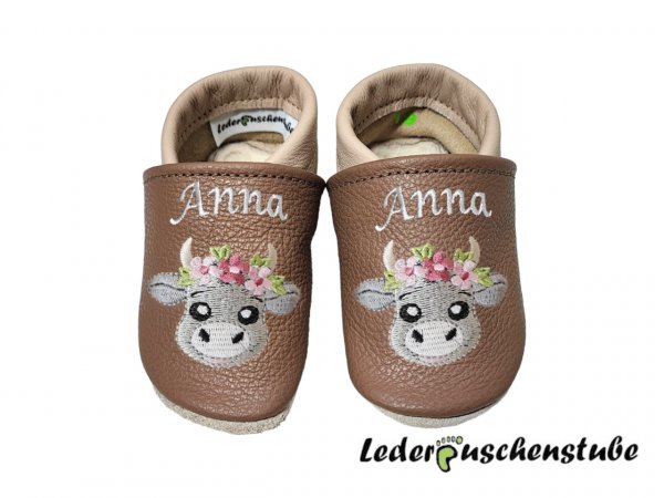 Lederpuschen cappuccino-beige mit beiderseits Namen am Spann (creme) und beiderseits Stickerei Boho Kuh (steingrau-grau, Blume rosa-altrosa, hellgrün)