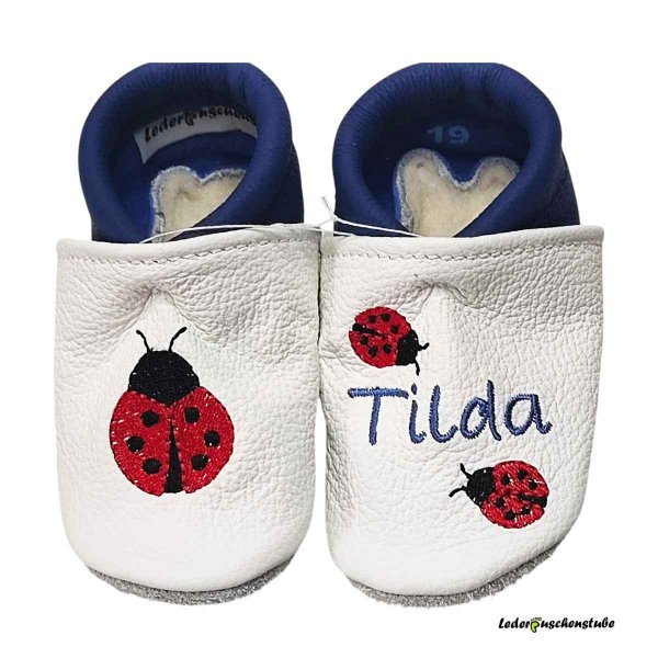 Krabbelschuhe in weiß-jeansblau, rechts großer Marienkäfer, links Namen jeansblau und 2 kleine Marienkäfer (rot-schwarz)