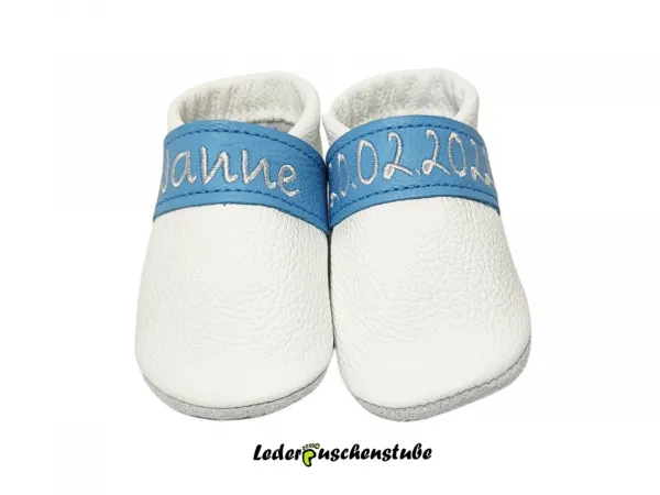 Lederpuschen als Taufschuh weiss, Spannband hellblau, rechts auf dem Spannband den Namen u. links das Tauf-o. Geburtsdatum (weiss)