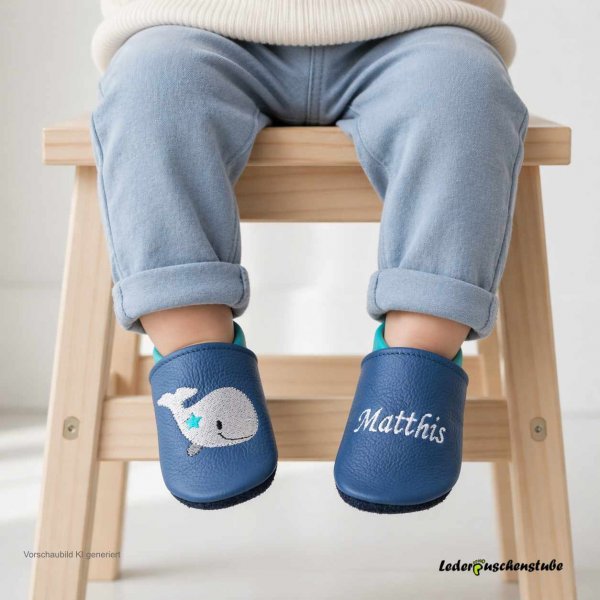 Getragene Babyschuhe Leder mit Namen – Lederpuschen jeansblau-türkis, rechts Wal mit Stern grau-anthrazit-schwarz-türkis, links Namen weiß (Vorschaubild KI-generiert an Babyfüßen)