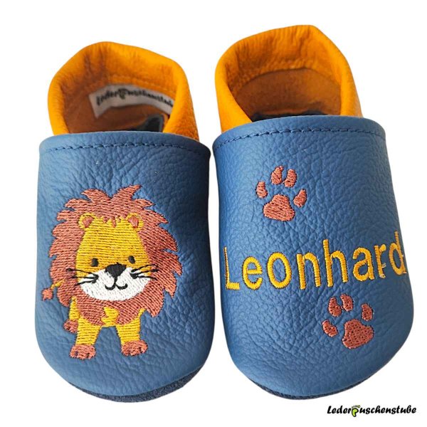 Krabbelschuhe in jeansblau-maisgelb, rechts Löwe steht (maisgelb-rotbrau-weiß-schwarz) und links Name (maisgelb) mit 2 Tatzen (rotbraun)
